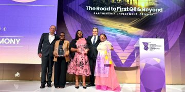 Five people stand on a stage posing with a glass trophy at the Namibia International Energy Conference 2026, with a purple backdrop reading 'The Road to First Oil & Beyond.'