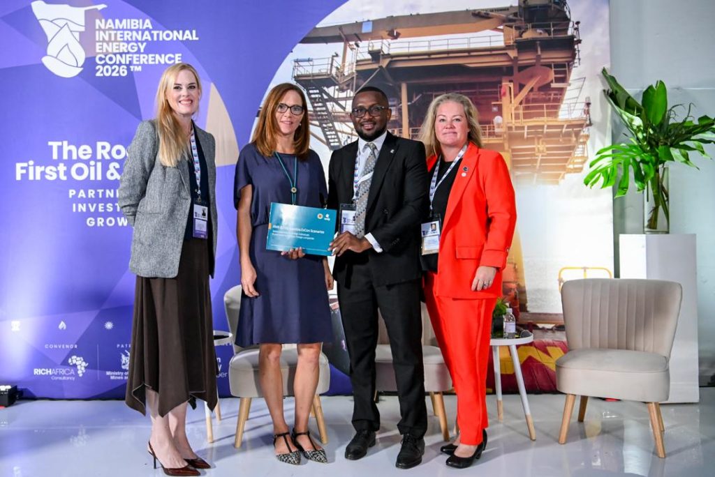 Group of four professionals on stage at the Namibia International Energy Conference 2026, with a blue backdrop and an award plaque held by the center-right man.