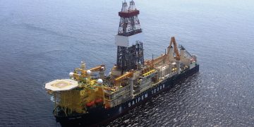 Offshore drilling vessel with a tall derrick and complex equipment on the deck, sailing in open ocean, labeled SAIPEM 12000 on the hull