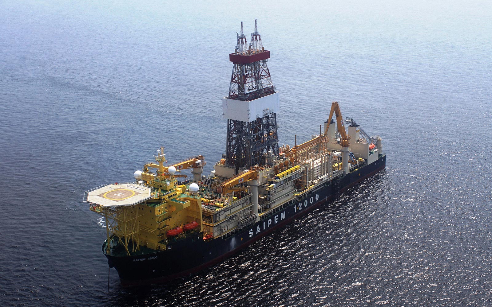 Offshore drilling vessel with a tall derrick and complex equipment on the deck, sailing in open ocean, labeled SAIPEM 12000 on the hull