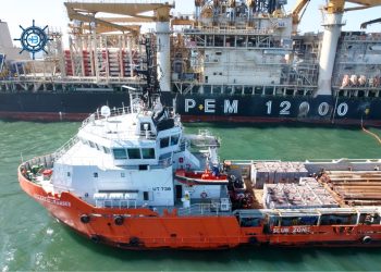 Orange and white rescue tugboat UT738, Atlantic Ranger, docked beside a large offshore support vessel with cranes in a harbor.