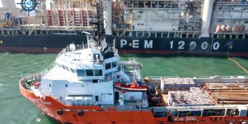 4d0b6604-e4f6-4167-95bb-9c9908498cbc | Mining and Energy Namibia | Namibia’s Leading Mining & Energy News Orange and white rescue tugboat UT738, Atlantic Ranger, docked beside a large offshore support vessel with cranes in a harbor.