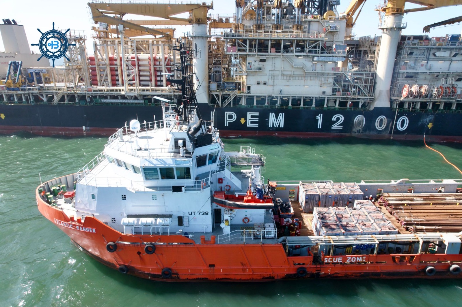 Orange and white rescue tugboat UT738, Atlantic Ranger, docked beside a large offshore support vessel with cranes in a harbor.