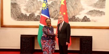 WhatsApp Image 2026-04-28 at 102116 AM | Mining and Energy Namibia | Namibia’s Leading Mining & Energy News Two dignitaries shake hands in a formal room, standing between Namibian and Chinese flags with a mountain landscape painting in the background.