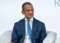 Robert Bose | Mining and Energy Namibia | Namibia’s Leading Mining & Energy News Man in a dark blue suit and light blue tie sits on a stage with a headset microphone, speaking at a panel discussion.