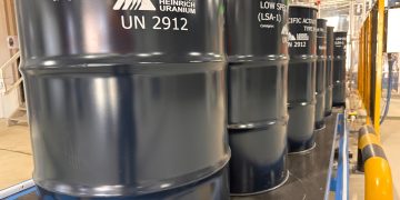 URANIUM OXIDE | Mining and Energy Namibia | Namibia’s Leading Mining & Energy News Row of dark blue industrial barrels labeled Low Specific Activity (LSA-1) UN 2912 in a factory setting near safety rails.