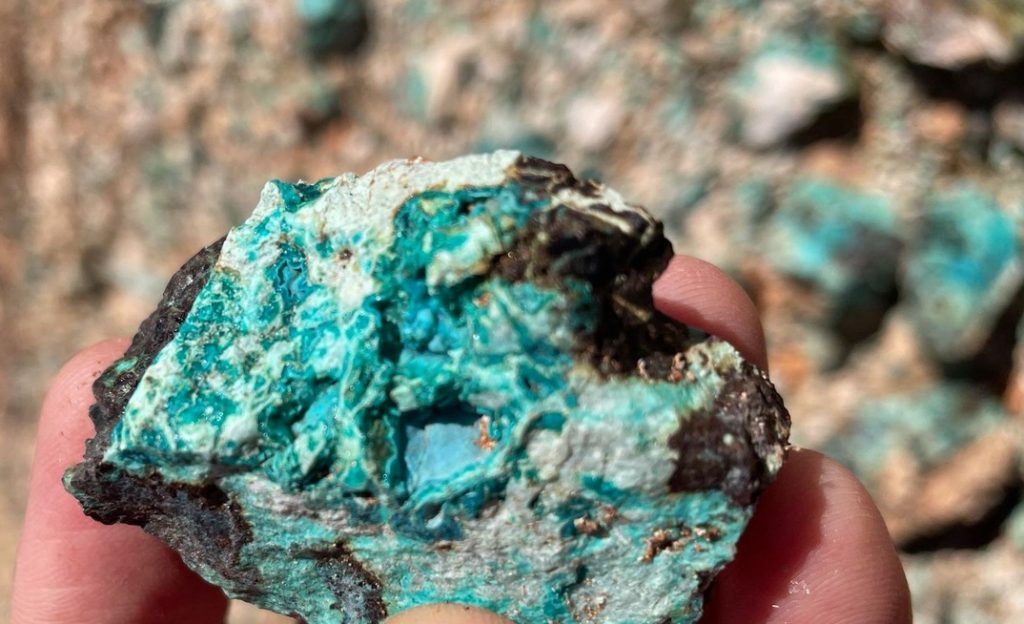 Turquoise-blue mineral sample held between two fingers, showing rough, mottled blue-green rock.