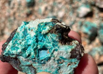 Turquoise-blue mineral sample held between two fingers, showing rough, mottled blue-green rock.