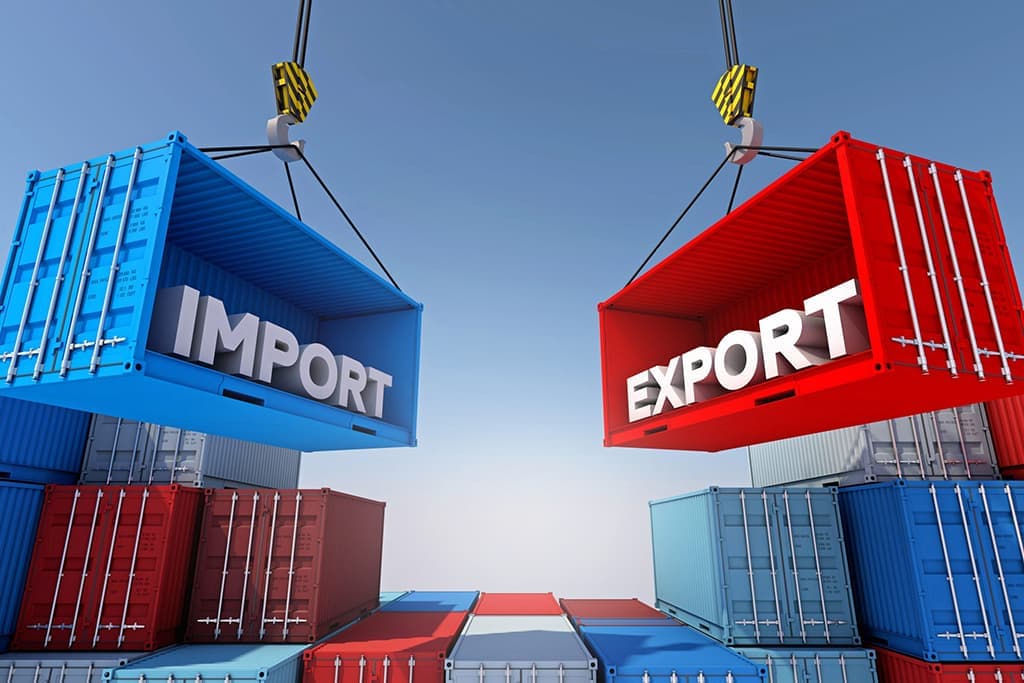 Two large shipping containers labeled IMPORT (blue) and EXPORT (red) are suspended by cranes above stacks of containers, illustrating trade.