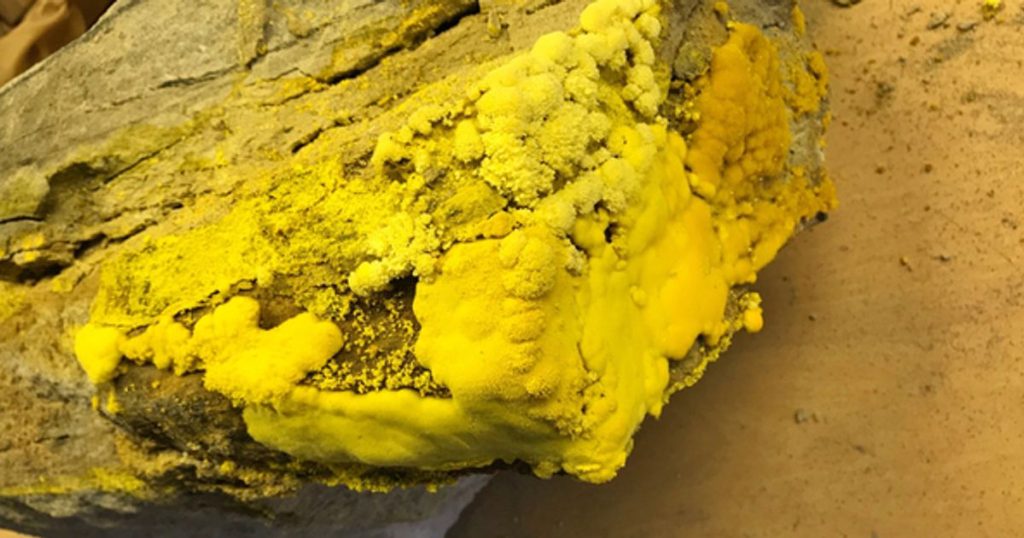 Rough rock surface covered in bright yellow sulfur mineral deposits.