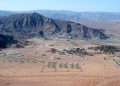 Rosh Pinah Zinc | Mining and Energy Namibia | Namibia’s Leading Mining & Energy News Desert valley with a cluster of green-roofed buildings at the base of rugged mountains, viewed from above.