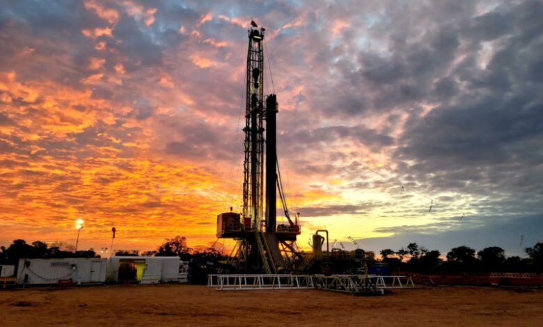 Oil drilling rig on a flat site at sunset, with an orange and purple sky behind it.