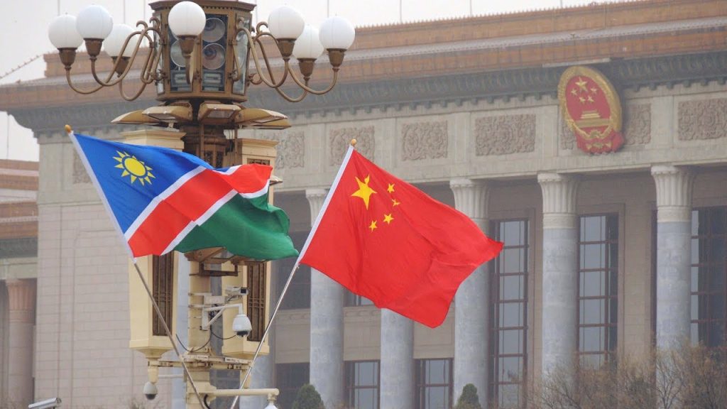 Namibia and China flags waving in front of a government building with columns, signaling international presence.