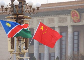 Namibia and China flags waving in front of a government building with columns, signaling international presence.