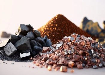 Piles of dark rocks and copper-colored mineral chunks on a light surface, with more mineral mounds blurred in the background.