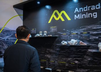 Person in a dark jacket observes a mining exhibit with labeled rock samples on a black wall reading 'Andrada Mining'.