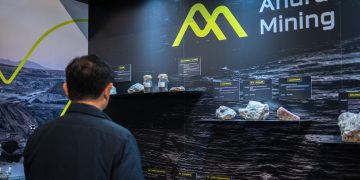 Person in a dark jacket observes a mining exhibit with labeled rock samples on a black wall reading 'Andrada Mining'.