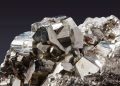 Cluster of metallic cubic pyrite crystals on a rocky matrix with shiny, reflective facets against a dark background.