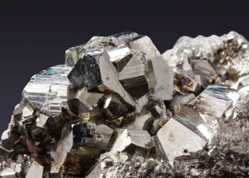 Cluster of metallic cubic pyrite crystals on a rocky matrix with shiny, reflective facets against a dark background.