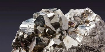 Cluster of metallic cubic pyrite crystals on a rocky matrix with shiny, reflective facets against a dark background.