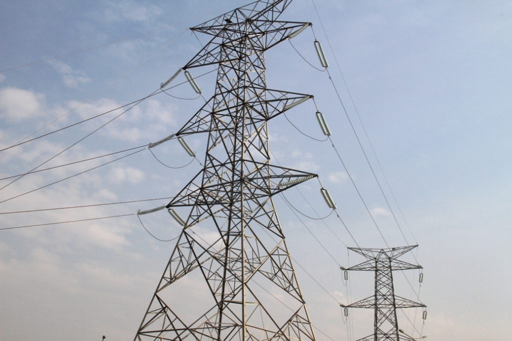 Industrial high-voltage power transmission tower with multiple wires against a blue sky, illustrating electricity infrastructure the power grid relies on.