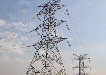 Industrial high-voltage power transmission tower with multiple wires against a blue sky, illustrating electricity infrastructure the power grid relies on.
