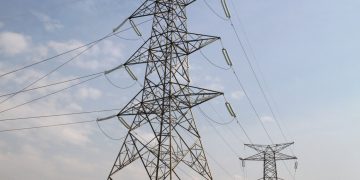 Industrial high-voltage power transmission tower with multiple wires against a blue sky, illustrating electricity infrastructure the power grid relies on.