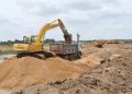 sand mining | Mining and Energy Namibia | Namibia’s Leading Mining & Energy News Yellow excavator loading sand into a dump truck at a dirt construction site, with more equipment lined up in the distance