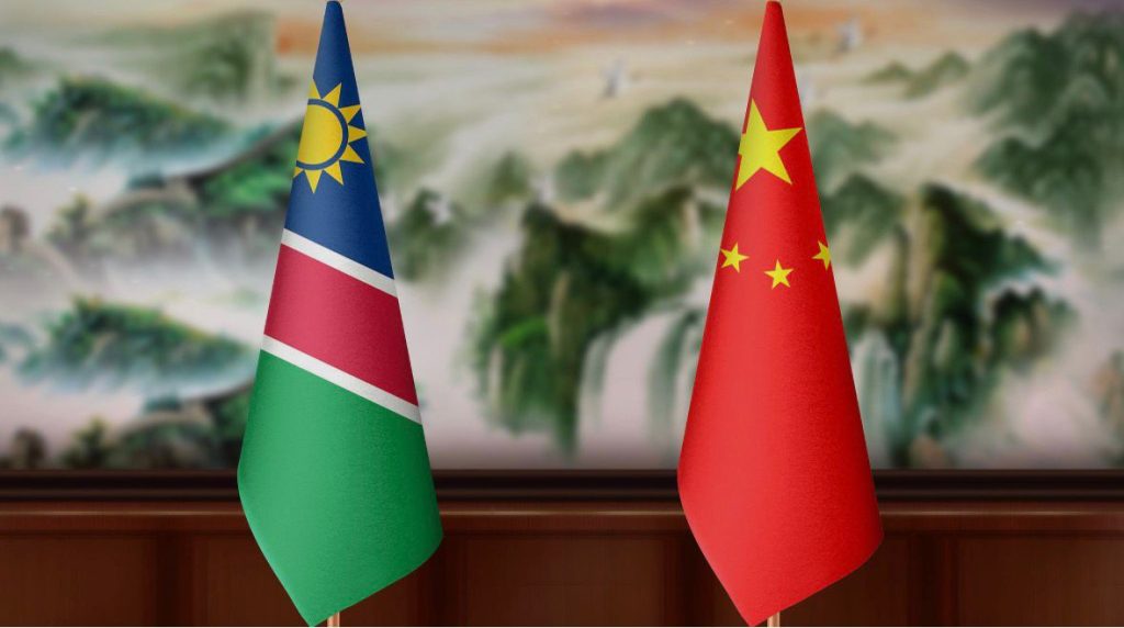 NAMCHINA | Mining and Energy Namibia | Namibia’s Leading Mining & Energy News Namibia and China flags on a wooden table against a blurred scenic backdrop.