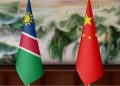 Namibia and China flags on a wooden table against a blurred scenic backdrop.