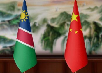 Namibia and China flags on a wooden table against a blurred scenic backdrop.