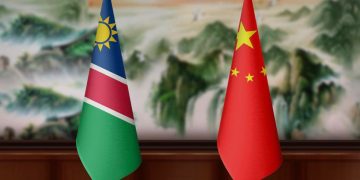 Namibia and China flags on a wooden table against a blurred scenic backdrop.