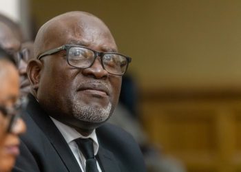 Close-up of an older Black man wearing glasses and a dark suit at a formal event.