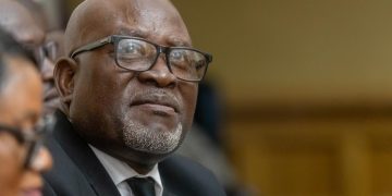 Close-up of an older Black man wearing glasses and a dark suit at a formal event.