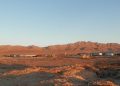 FORSYS | Mining and Energy Namibia | Namibia’s Leading Mining & Energy News Desert settlement with low buildings and storage containers on a rocky plain, mountains in the distance at sunset.