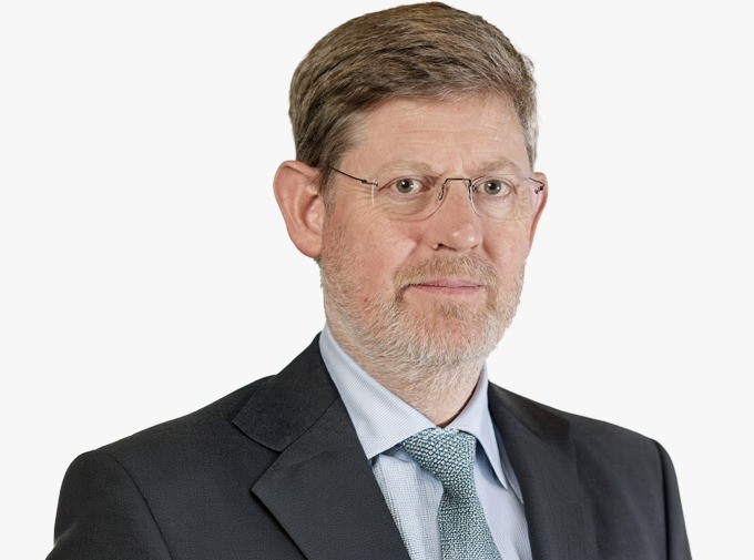 Portrait of a middle-aged man with glasses, gray beard, wearing a dark suit and light blue shirt with a teal tie, looking at the camera.