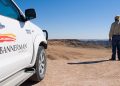 White pickup truck with Bannerman Resources branding in the desert, a man in a hat stands at the edge looking over arid hills under a blue sky.