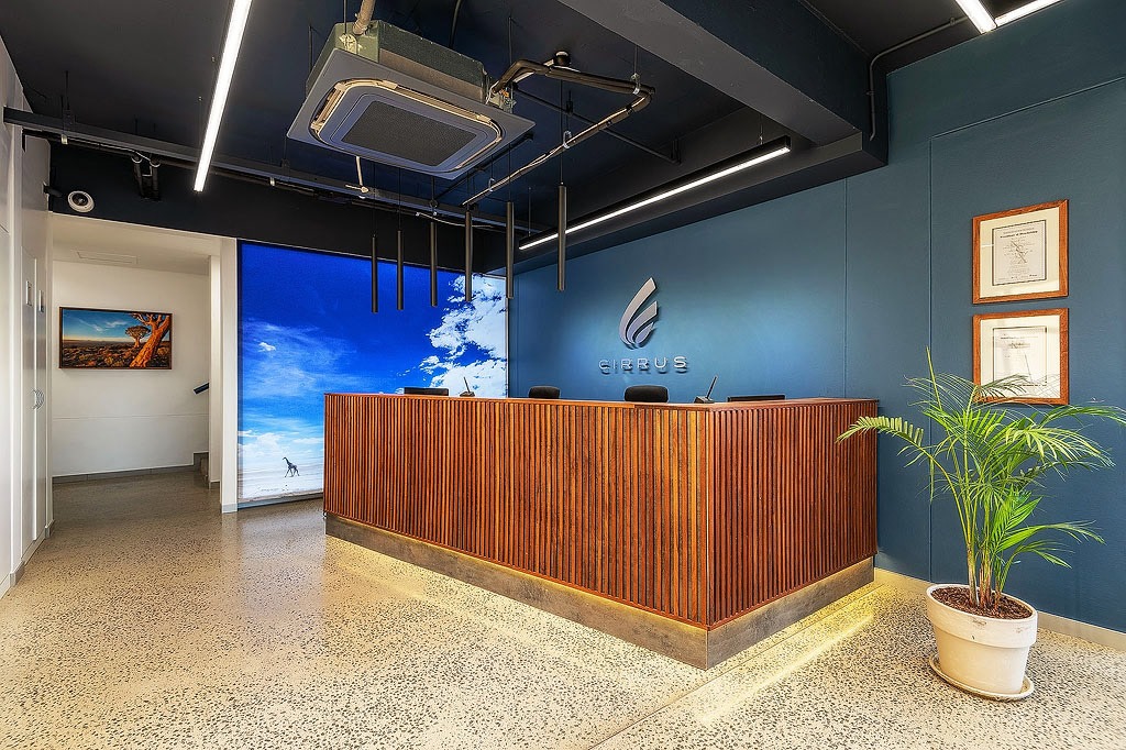 NSX sponsor | Mining and Energy Namibia | Namibia’s Leading Mining & Energy News Reception desk in a modern office lobby with a blue wall and company logo, wood-panel front, and a potted plant nearby.