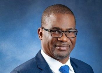 Eugene Okpere | Mining and Energy Namibia | Namibia’s Leading Mining & Energy News Professional headshot of a man wearing a navy suit and blue tie, glasses, against a blue studio backdrop.