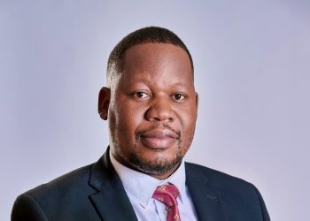 Nicholas Mukasa | Mining and Energy Namibia | Namibia’s Leading Mining & Energy News Professional headshot of a man in a dark suit, light blue shirt, and red tie against a neutral gray background.