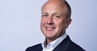 Portrait of a smiling man in a dark suit and white shirt facing the camera (head-and-shoulders).
