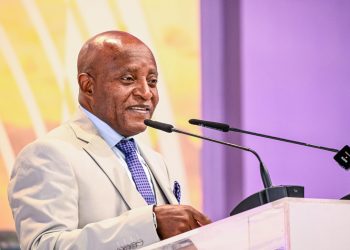 ELIJAH NGURARE | Mining and Energy Namibia | Namibia’s Leading Mining & Energy News A man in a light suit and blue tie speaks at a podium with two microphones in front of a colorful backdrop