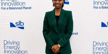 Professional woman in a dark green blazer posing in front of a white backdrop with 'Driving Energy Innovation' slogan and SLB logos.