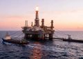WhatsApp Image 2026-06-21 at 82437 AM | Mining and Energy Namibia | Namibia’s Leading Mining & Energy News Offshore oil rig with a tall flare stack at sunset, connected to two escort ships in calm sea.