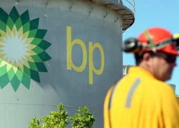 BP logo on a large cylindrical storage tank with a worker in yellow safety gear in the foreground against a blue sky.