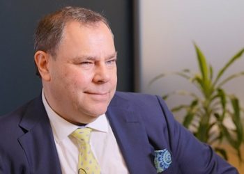 Jeremy Asher | Mining and Energy Namibia | Namibia’s Leading Mining & Energy News Man in a navy suit and yellow patterned tie sits in an office, with a plant in the background and a calm, thoughtful expression.