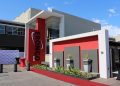 Modern building entrance for a corporate event, with a red carpet, red accent wall, and a tall vertical sign beside the doorway reading EONCO (brand).