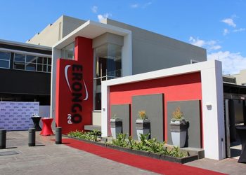 Modern building entrance for a corporate event, with a red carpet, red accent wall, and a tall vertical sign beside the doorway reading EONCO (brand).