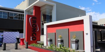 Modern building entrance for a corporate event, with a red carpet, red accent wall, and a tall vertical sign beside the doorway reading EONCO (brand).