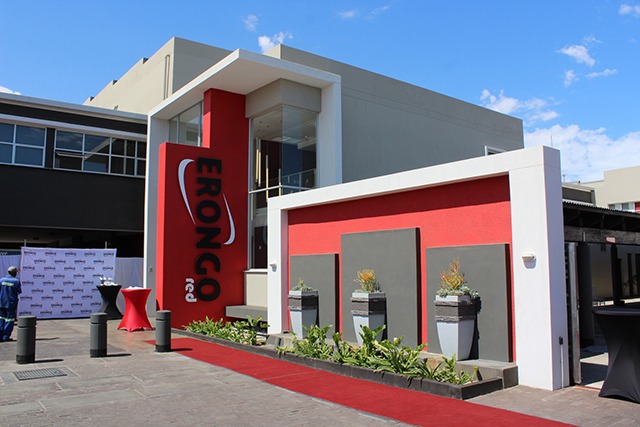 Modern building entrance for a corporate event, with a red carpet, red accent wall, and a tall vertical sign beside the doorway reading EONCO (brand).